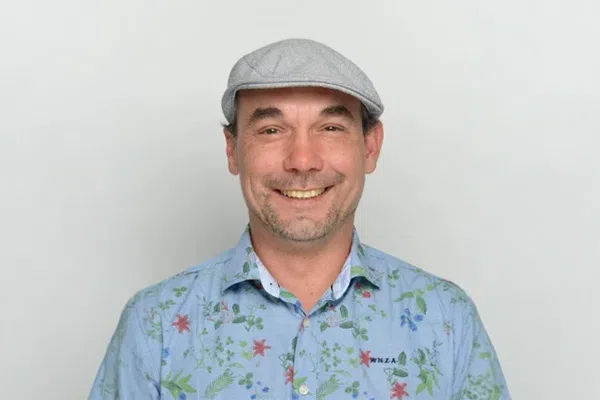 Kai Uwe Vogel mit Schirmmütze und blauem Hemd mit floralem Muster lächelt vor weißem Hintergrund.