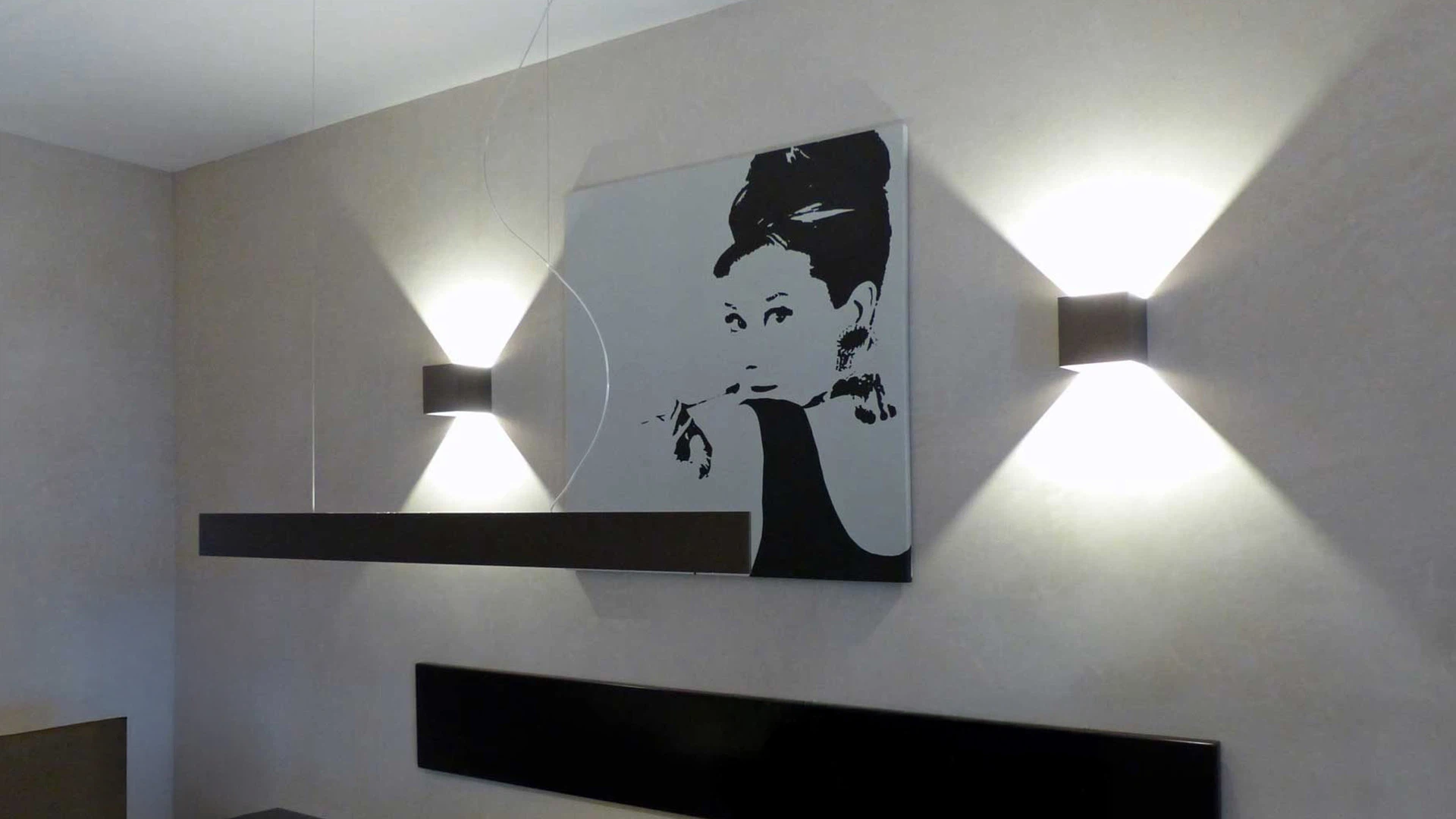 Schwarz-weißes Wandbild einer Frau in einem stilvollen, minimalistisch eingerichteten Raum mit zwei modernen Wandlampen.