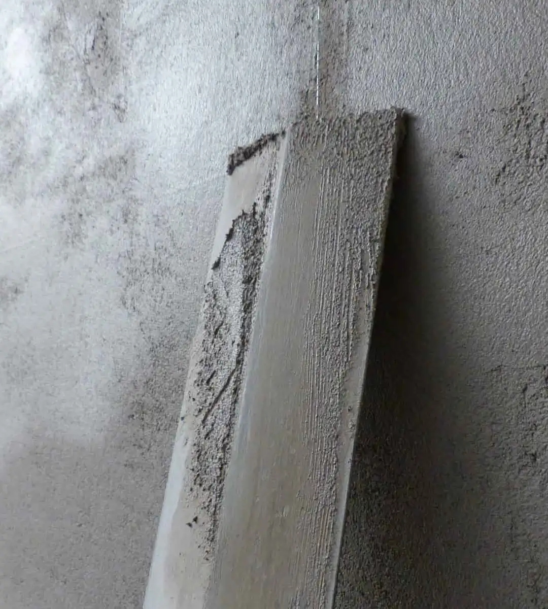 Nahaufnahme einer grauen Wand mit feuchtem Putz, der auf einem Holzbrett verteilt ist.