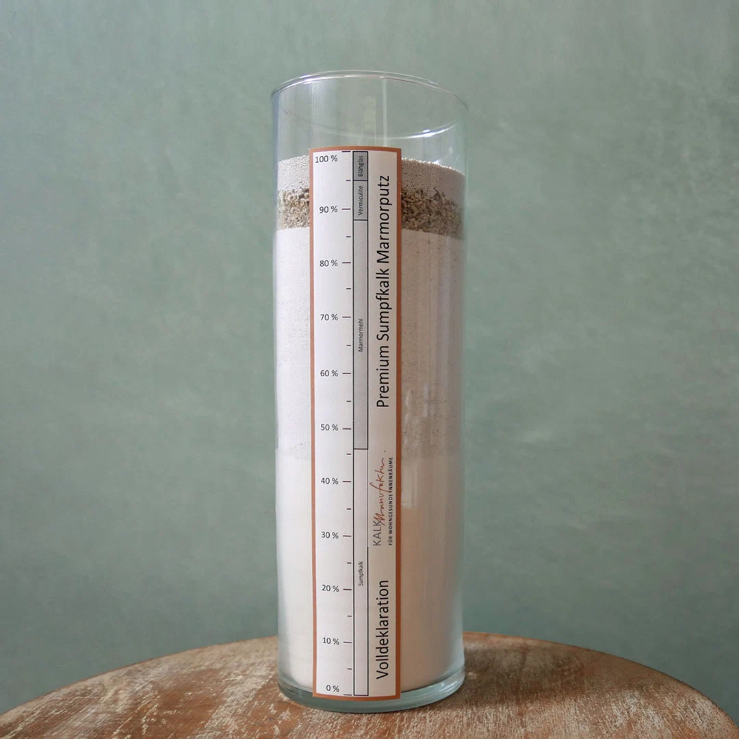 Glaszylinder mit geschichteten Pulvern und Körnern, beschriftet mit Anteilen von Sumpfkalk, Marmormeh und Vermiculite für Premium Sumpfkalk Marmorputz.