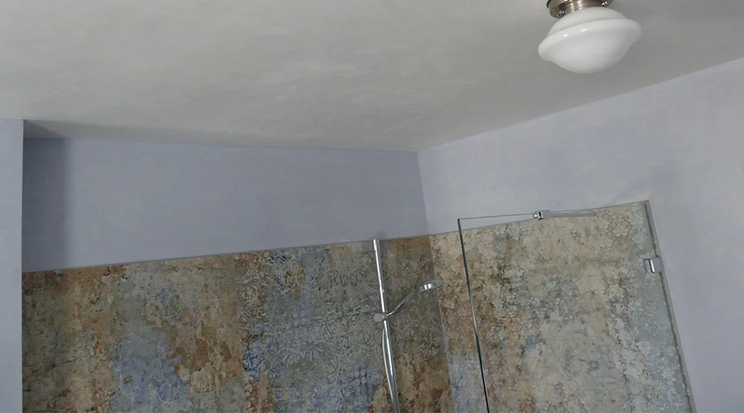 Badezimmer mit einer Duschkabine aus Glas, einer silbernen Duschstange und einer Wand mit blaugrauen und beigen Marmorfliesen.