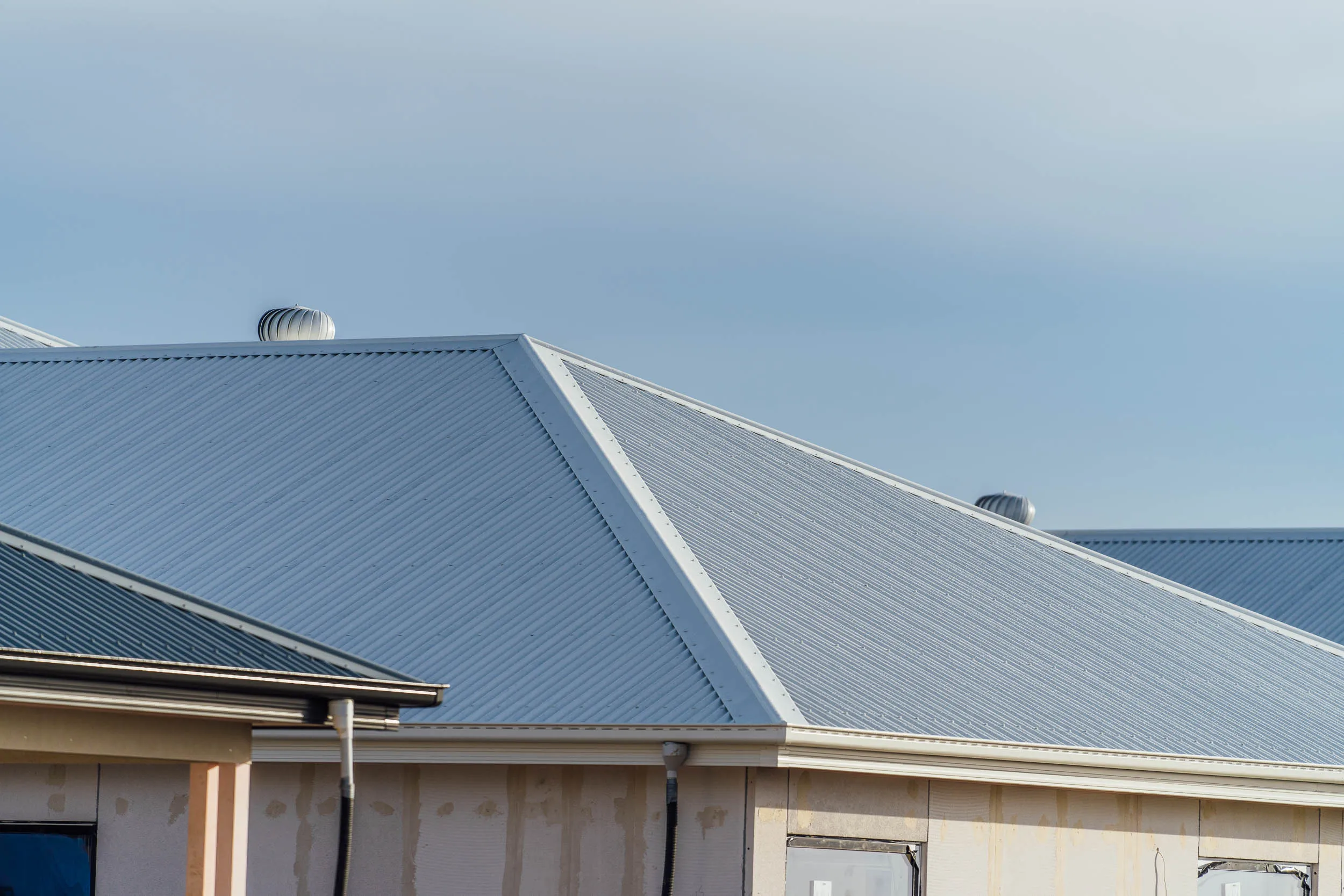 Close-up of a building's corrugated metal roof and vent turbines against a clear sky.