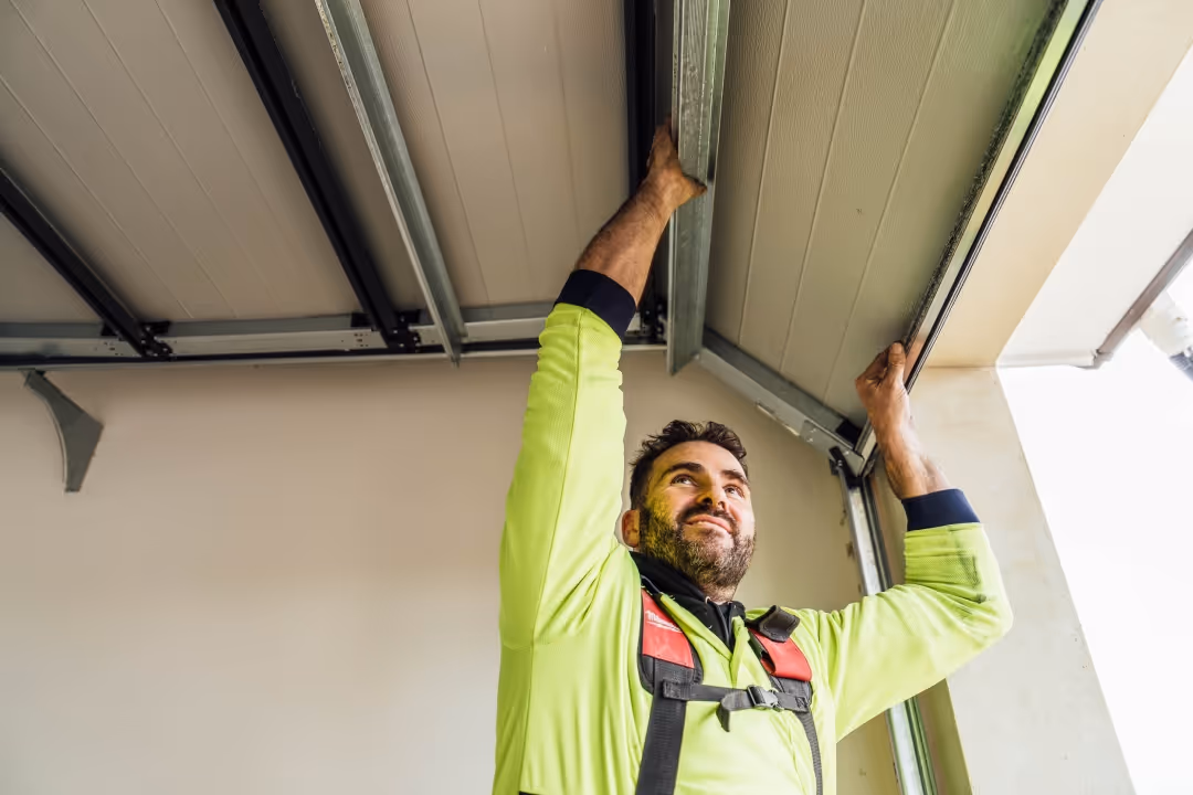 Worker in safety gear installing or fixing a metal garage door panel from inside.