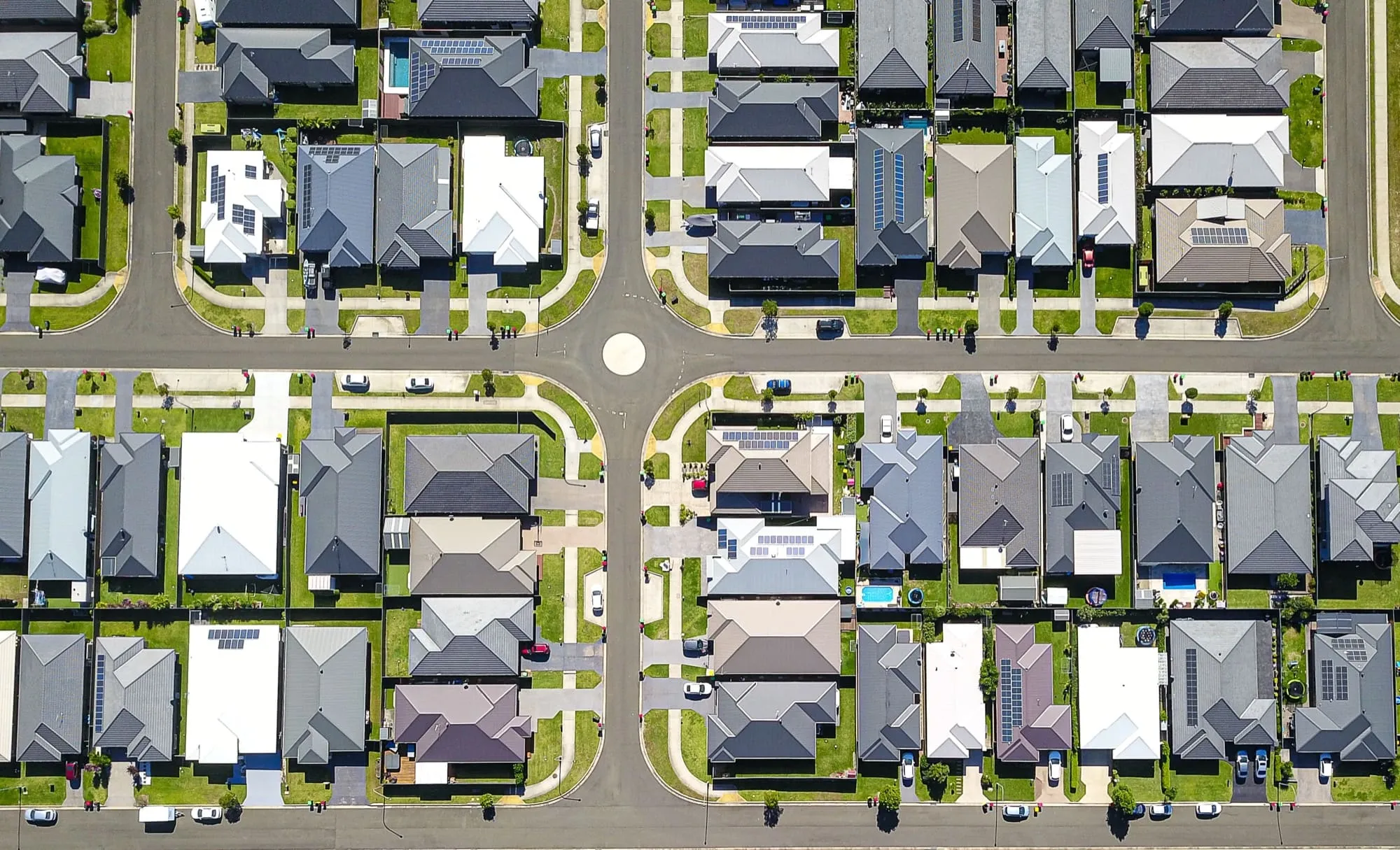 Aerial view of a suburban neighborhood with houses, roads, roundabout, and green lawns.