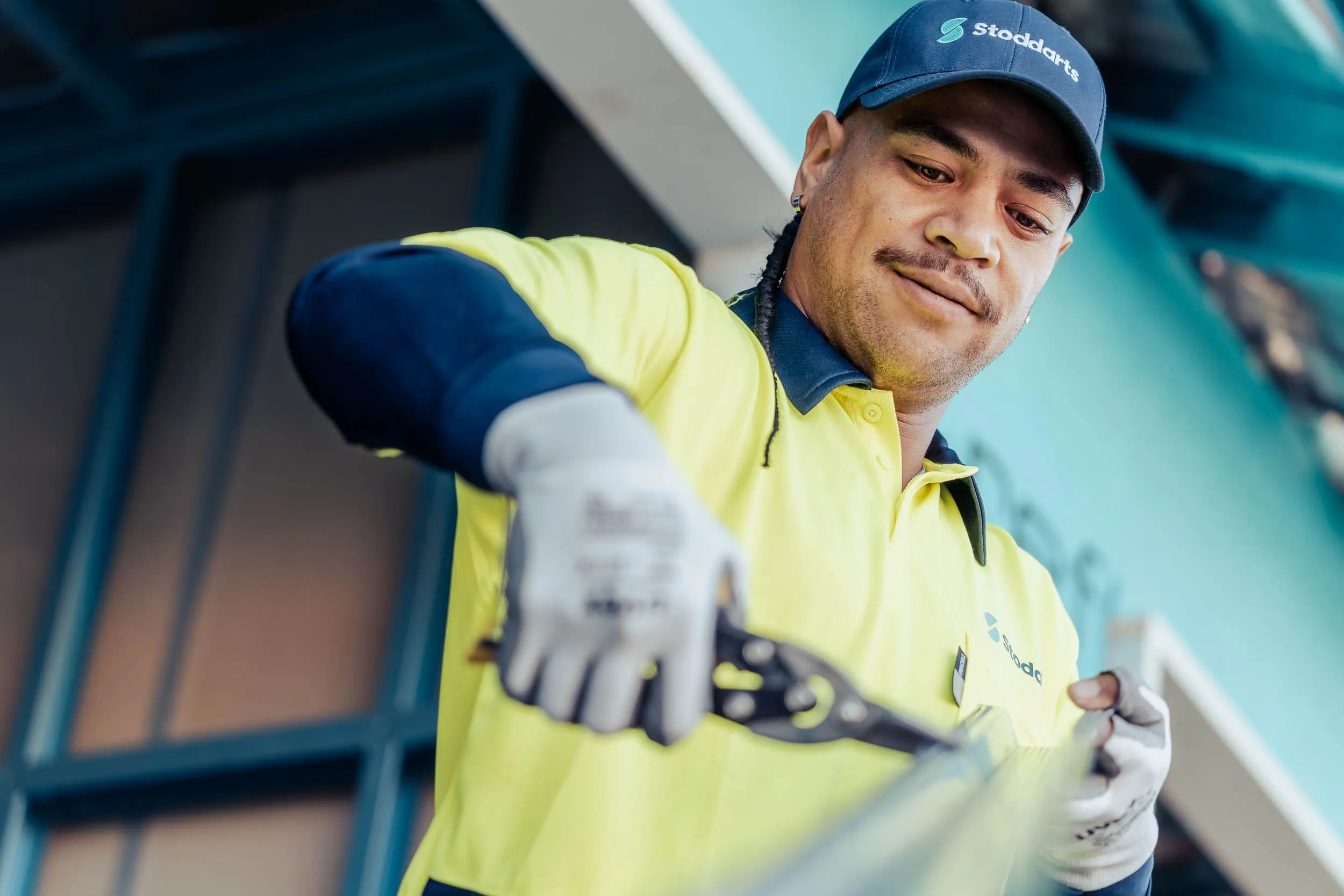 Worker in yellow Stoddarts uniform using snips to cut metal in an industrial setting.