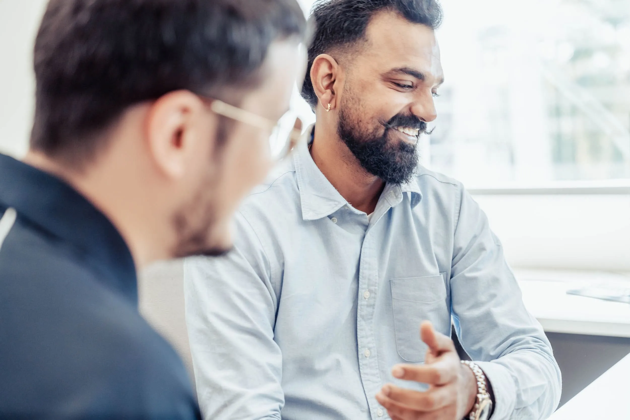 Two men having a friendly conversation in a bright office setting, one smiling and gesturing.