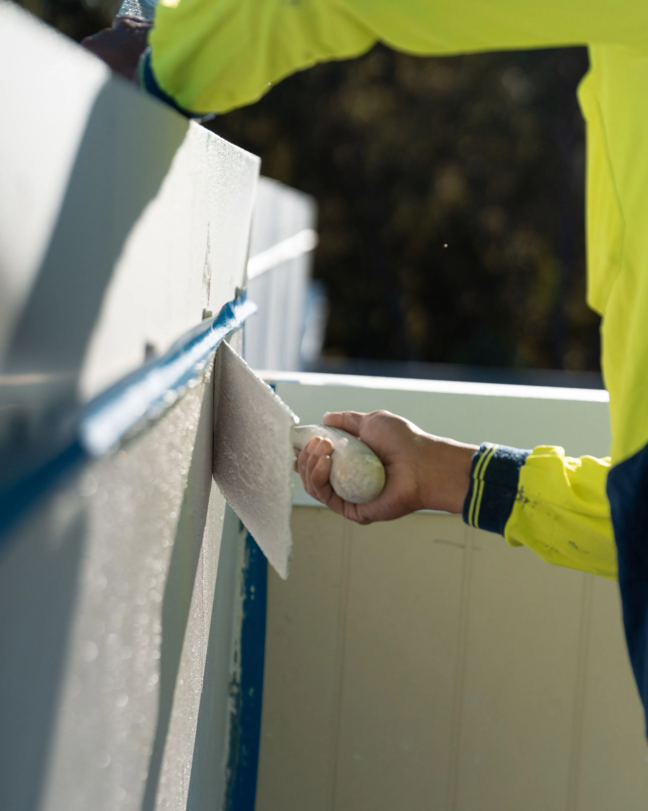 Person in yellow jacket applying plaster or cement to a wall with a trowel.