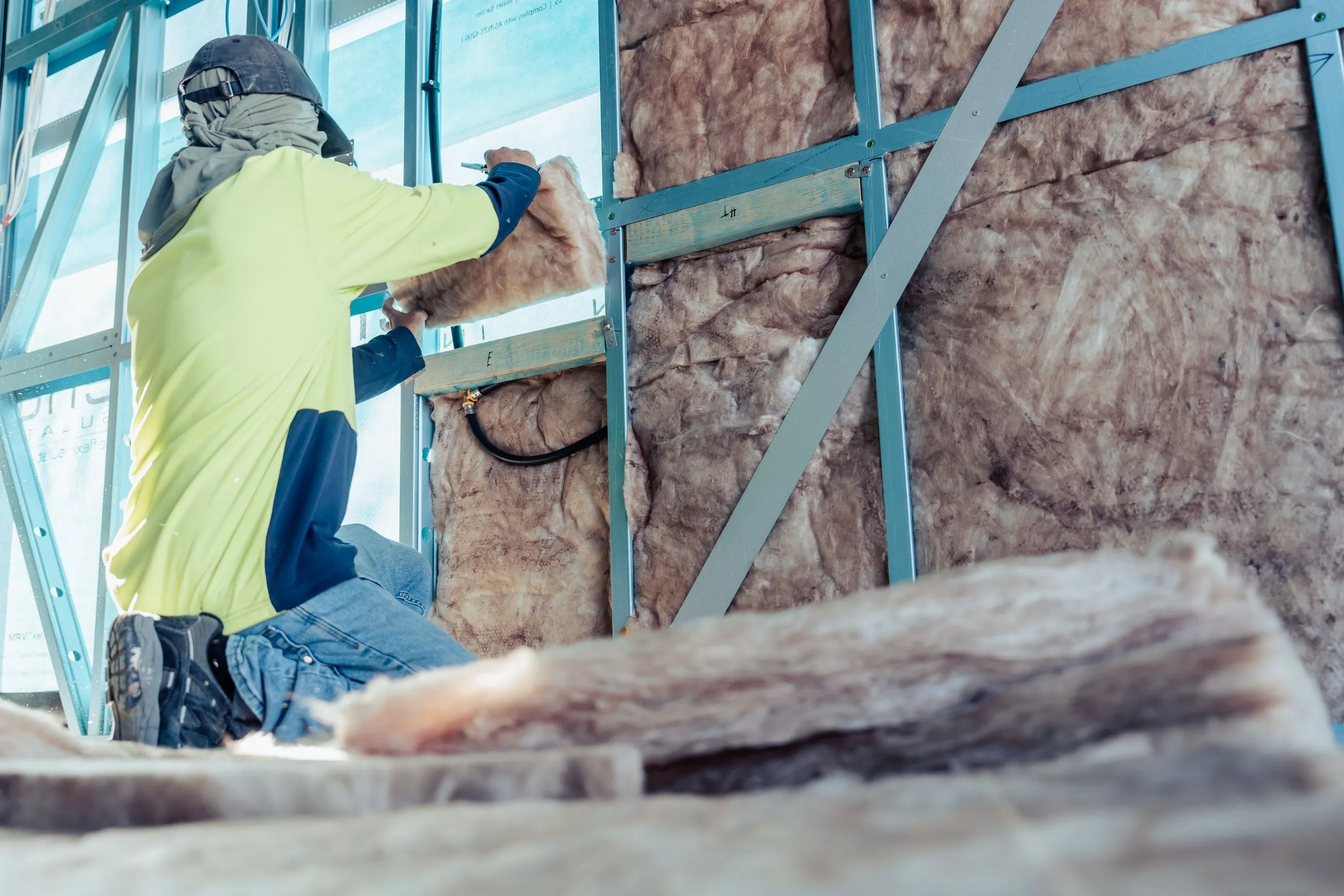 Worker wearing safety gear installs insulation panels in a building wall frame.