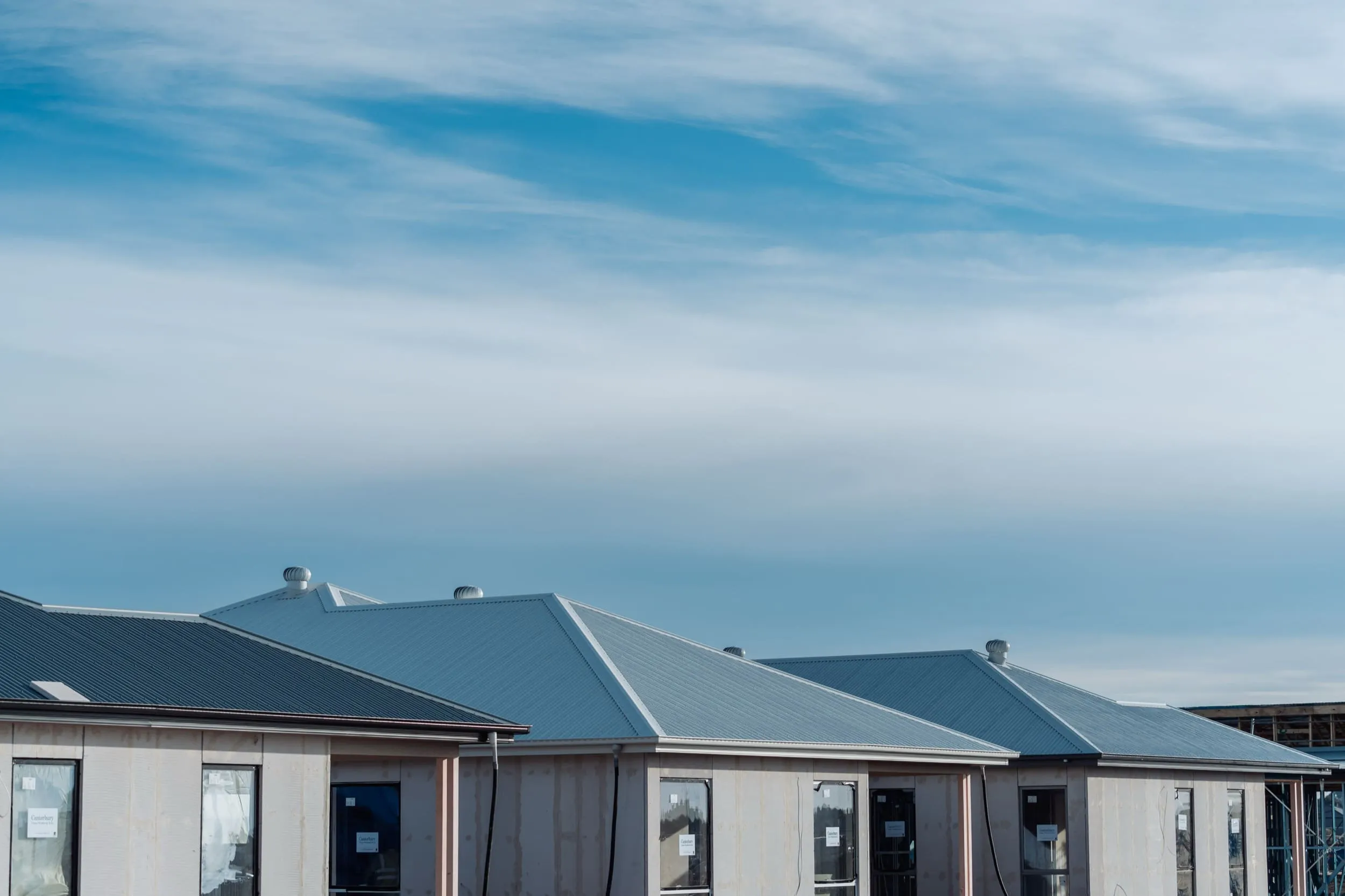 Row of houses under construction with metal roofs against a partly cloudy blue sky.