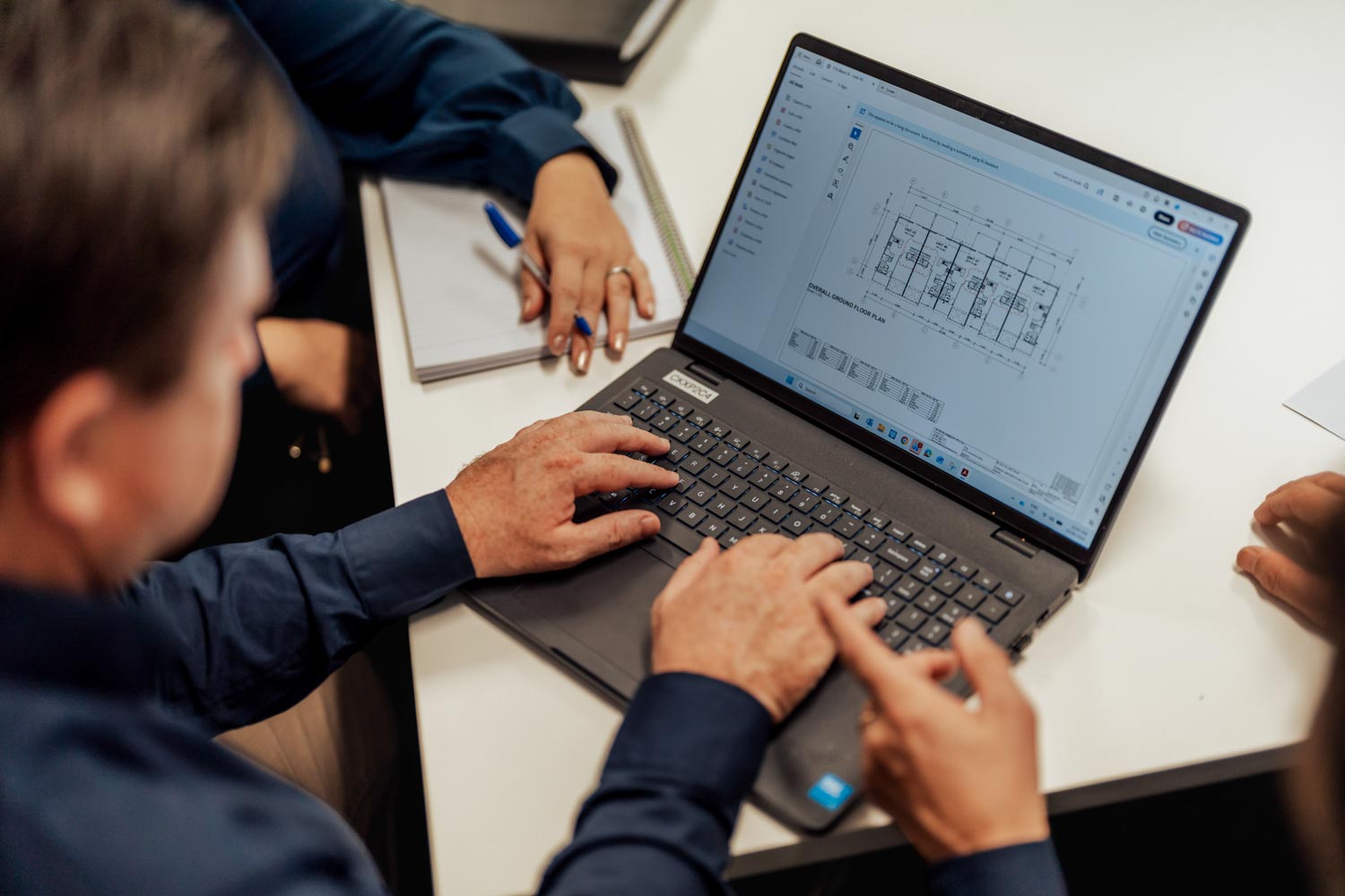 People reviewing a building floor plan displayed on a laptop at a white desk.