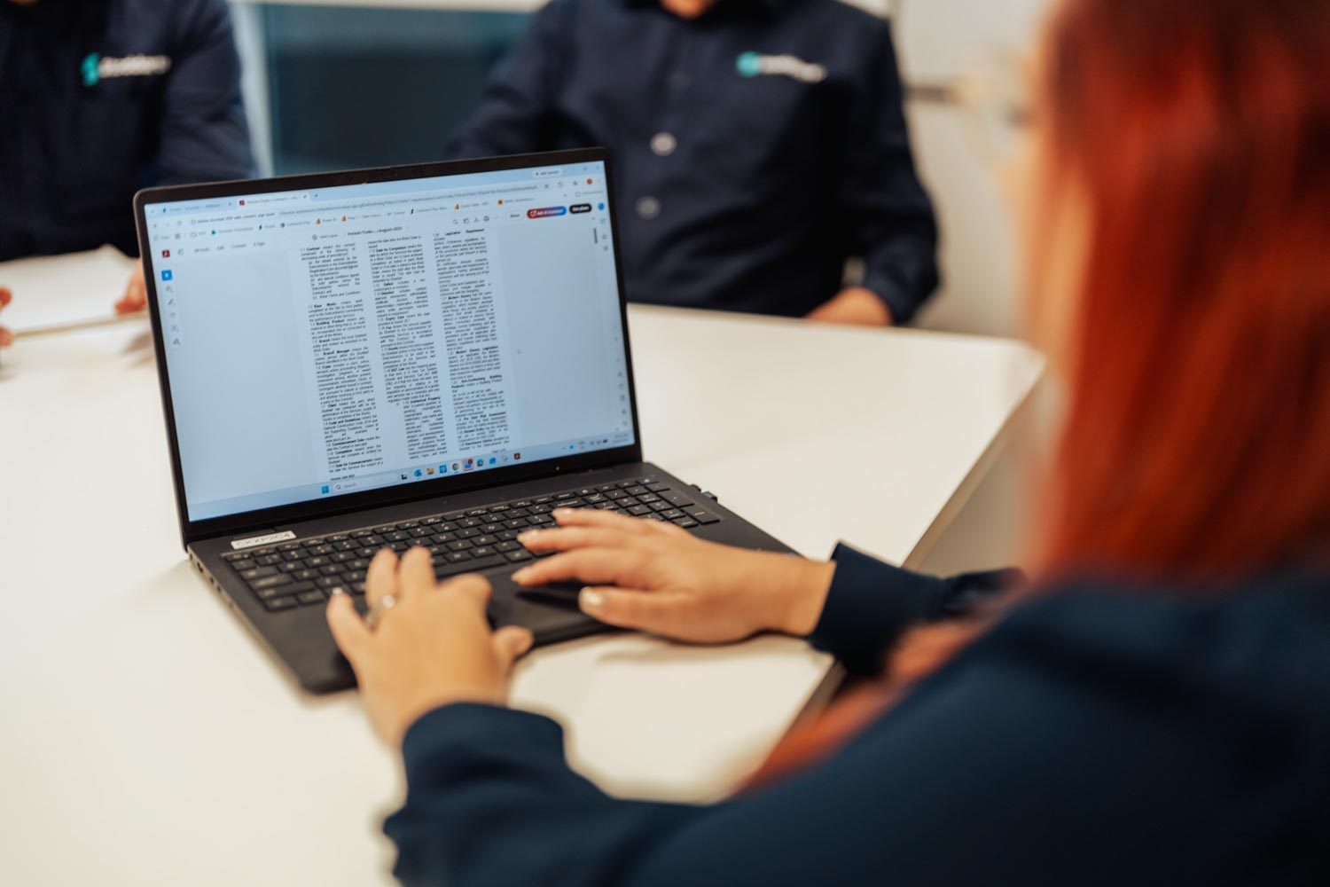 Person typing on a laptop showing a multi-column document on screen in a meeting room.