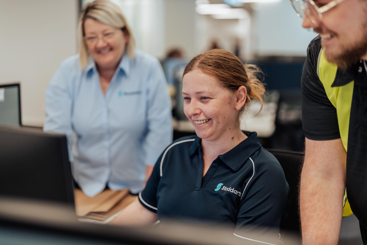 Three smiling coworkers collaborating around a computer in an office environment.