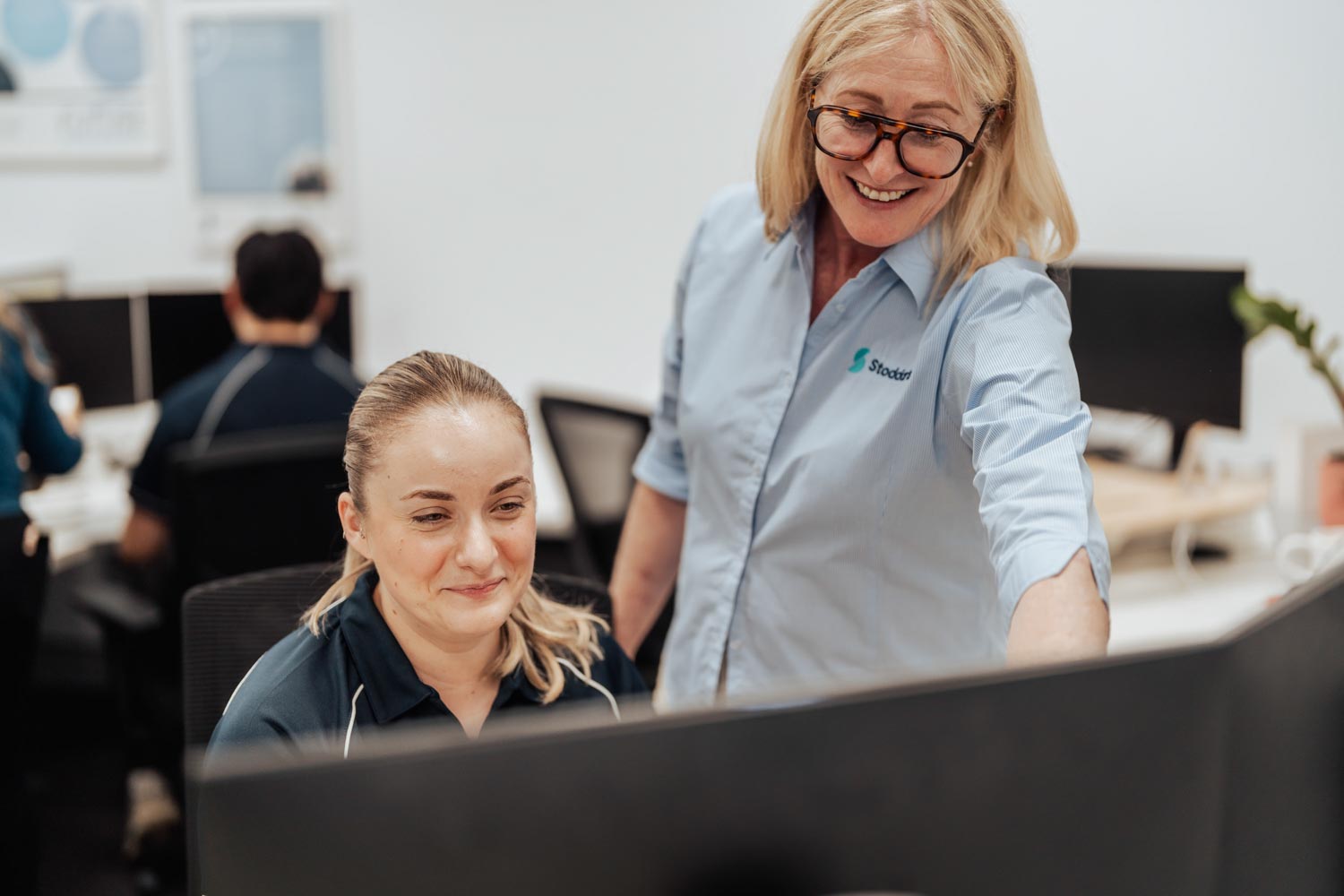 Two women collaborating and looking at a computer screen in a bright office space.