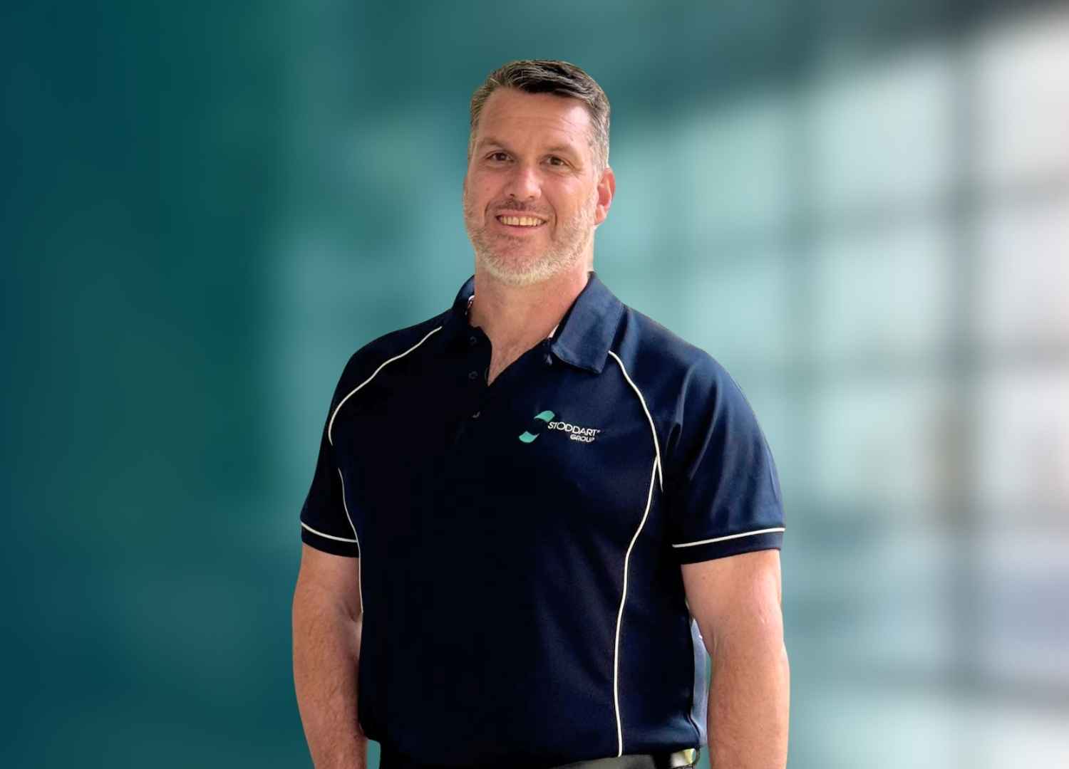 Smiling man with short hair and beard wearing a navy polo shirt with the Stoddart Group logo.