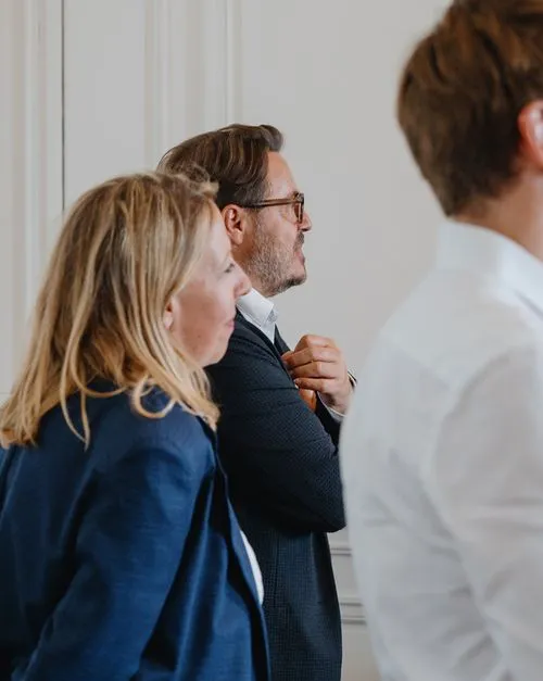 Trois personnes debout, deux regardant vers la droite, une en avant-plan floue.