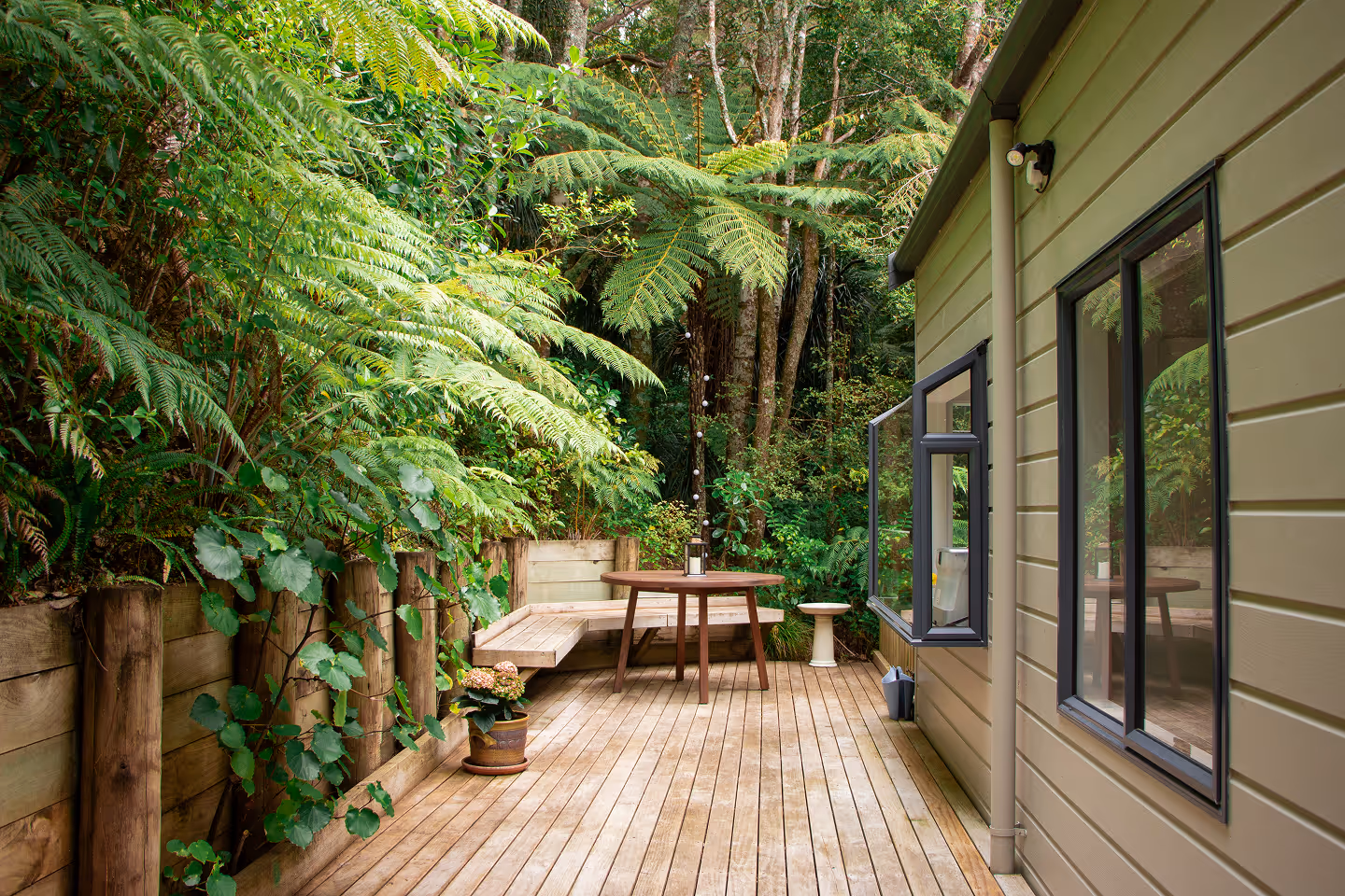 Private outdoor deck with seating area overlooking native New Zealand bush, perfect for relaxing at an Auckland short-term rental.
