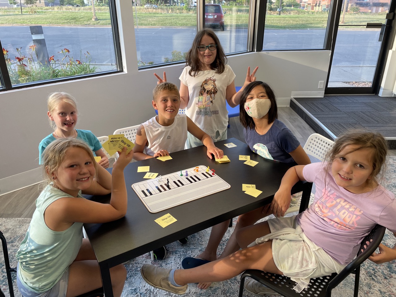 A kid playing piano while other kids on the background are watching him at a group piano lesson
