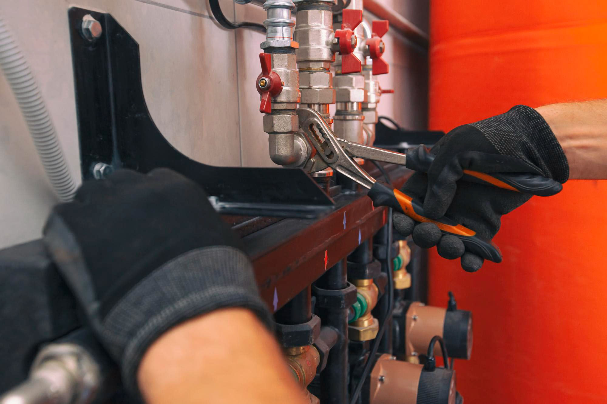 Person using a wrench to adjust plumbing pipes, wearing gloves for safety.