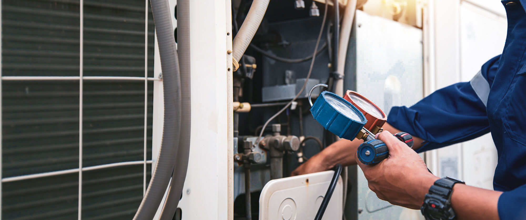 A technician uses gauges to check a large outdoor air conditioning unit.