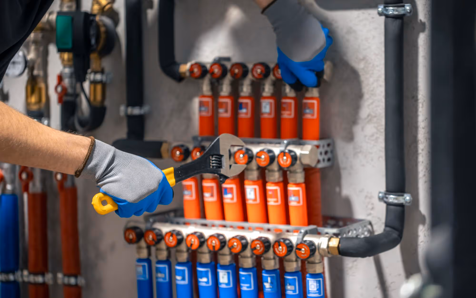 A person in gloves uses a wrench to adjust valves on a pipe system.