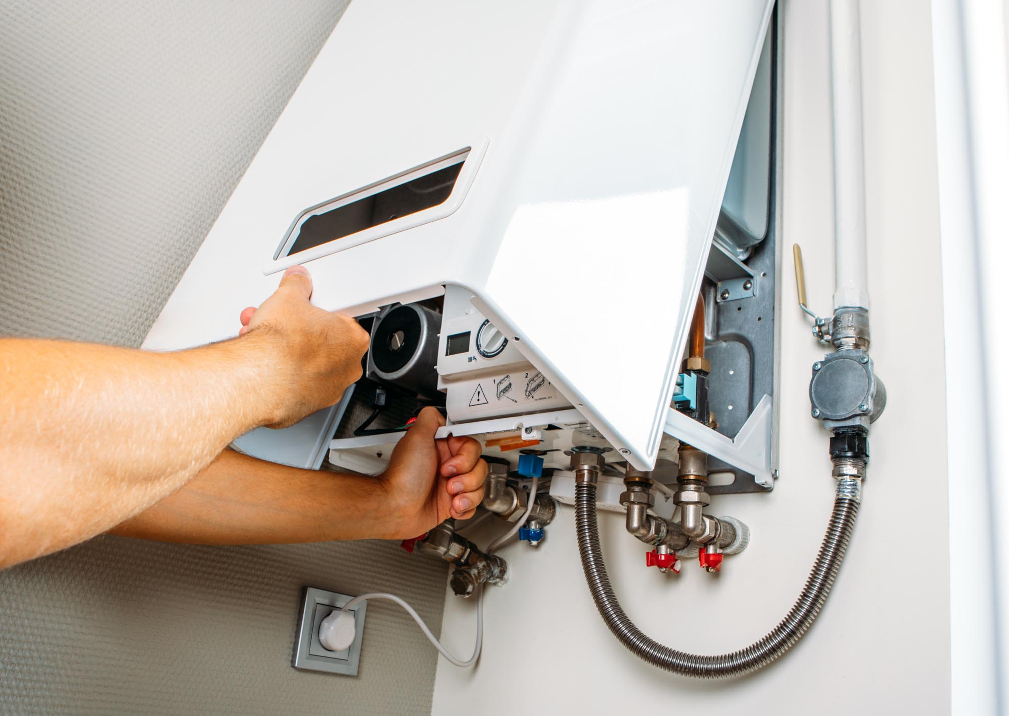 A person repairs an open wall-mounted boiler, adjusting internal components and checking connections.