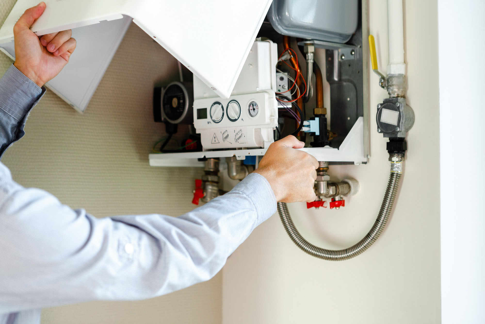 A person adjusts settings on a wall-mounted boiler with exposed internal components.