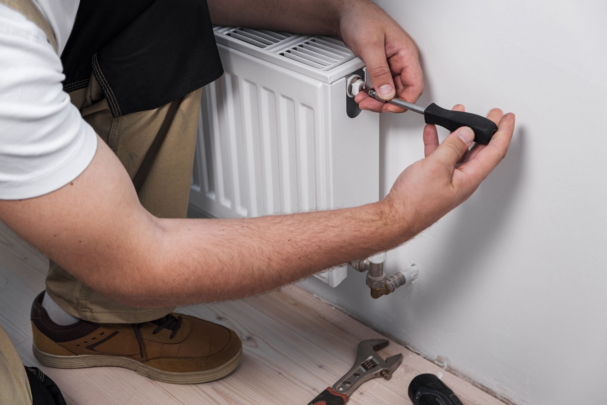 Person using a screwdriver to adjust a valve on a white radiator attached to a wall.