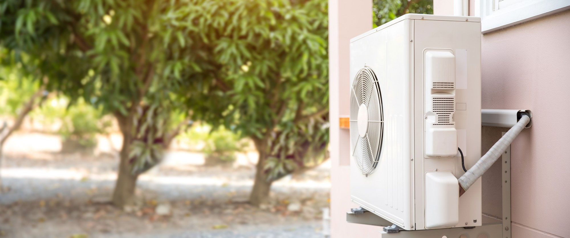 Air conditioning unit installed on an outdoor wall with trees visible in the background.