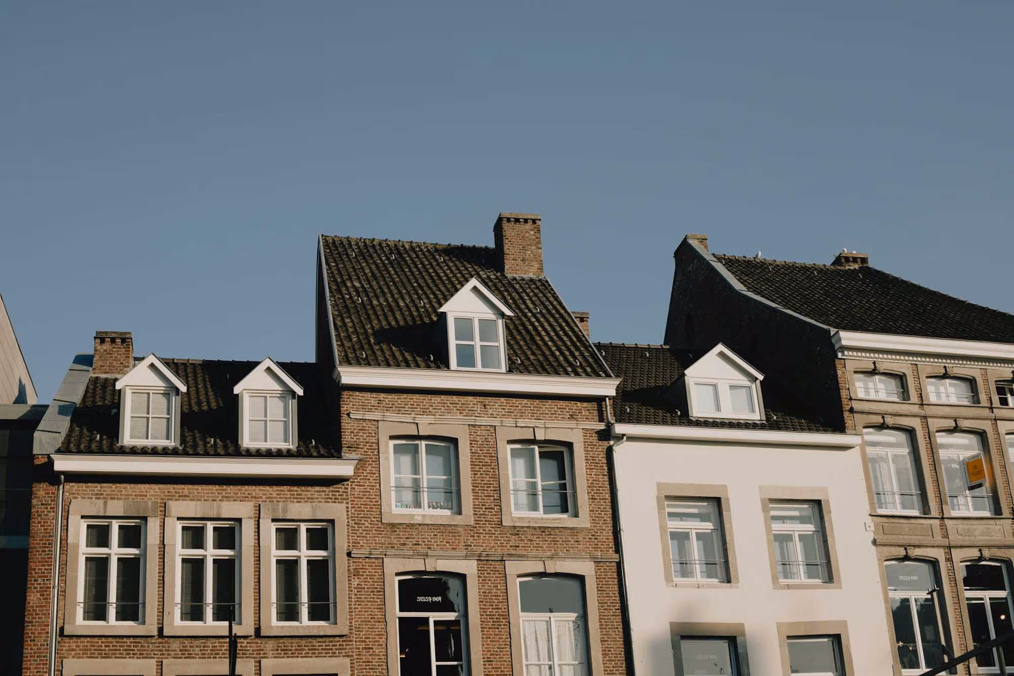 Three adjacent brick houses with chimneys under a clear blue sky.