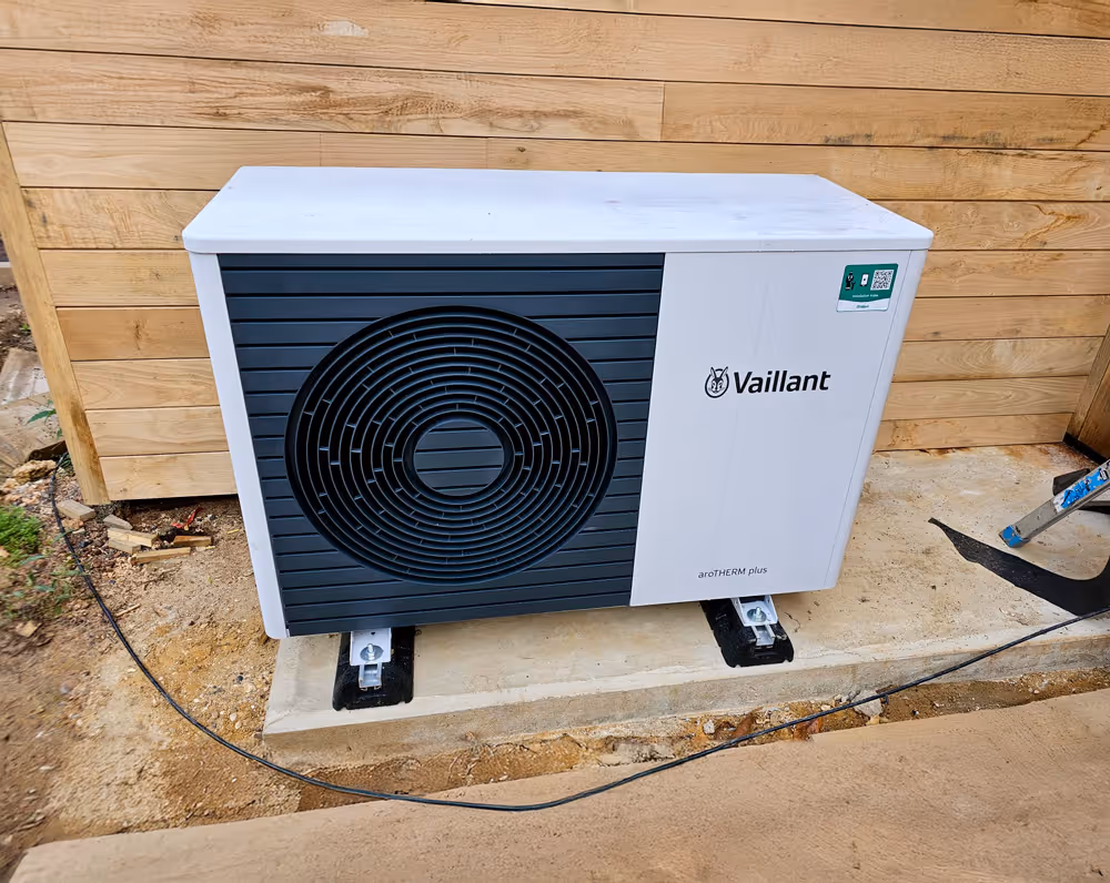 Outdoor air conditioning unit mounted on a concrete slab beside a wooden wall.