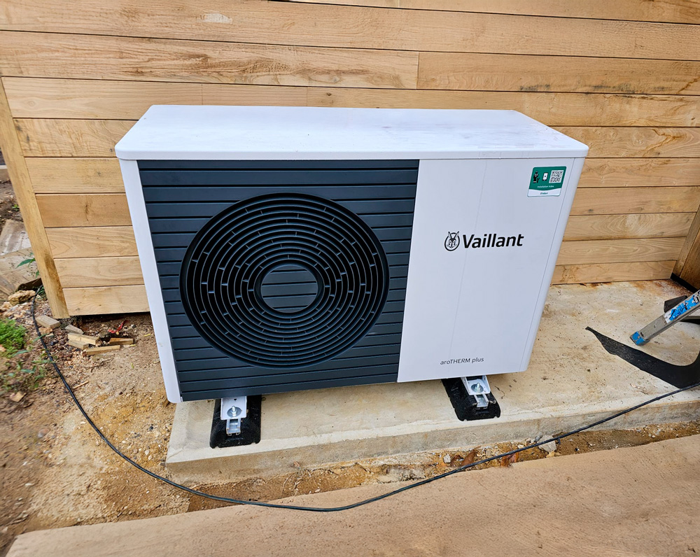 Outdoor air conditioning unit mounted on a concrete slab beside a wooden wall.