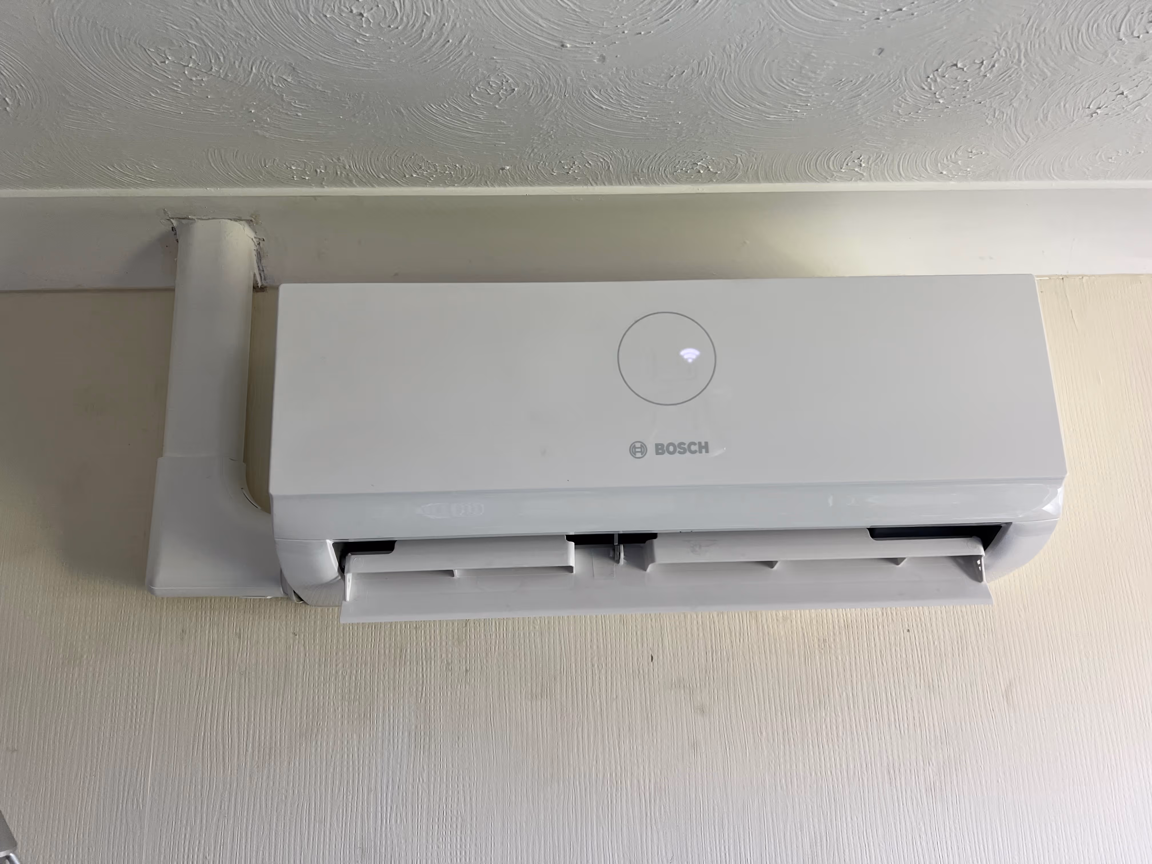 Wall-mounted air conditioning unit with a circular light on top, installed near the ceiling.