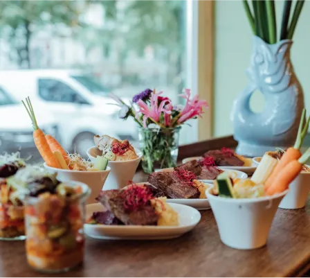 Vielfältige Auswahl an warmen Speisen und Fingerfood auf modernen Tellern, dekoriert mit frischen Blumen – Catering-Angebot in Hamburg.