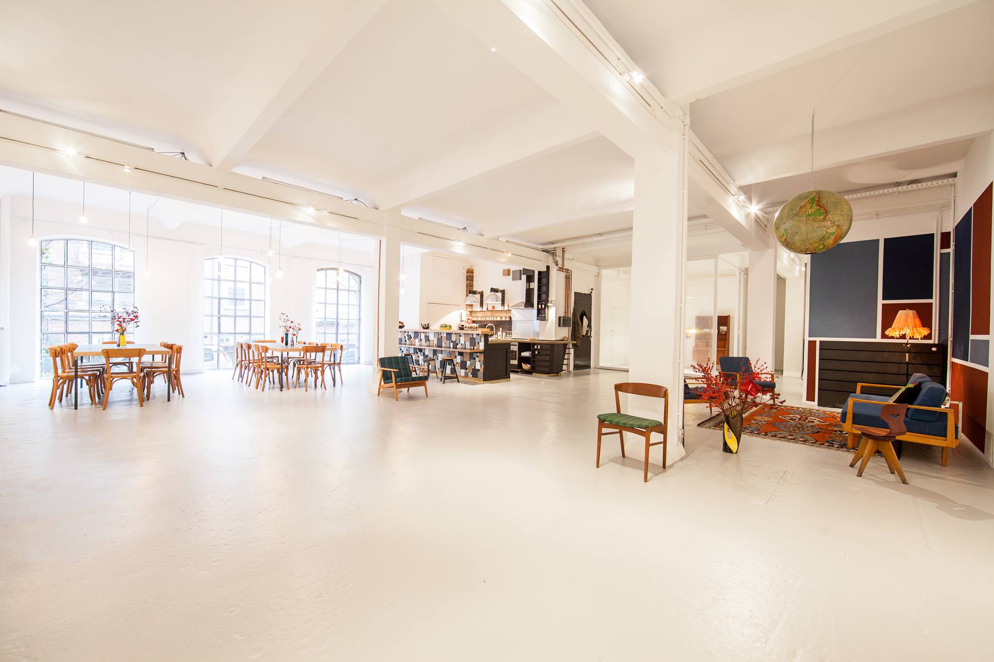 Weitwinkelaufnahme Loft 1 – 200 m² großes Studio mit hohen Decken, hellem Boden, mehreren Tischen, Sofas und moderner Einrichtung.