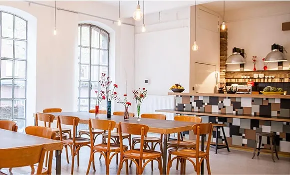 Heller Veranstaltungsraum mit Holztischen, Stühlen und offener Küche – Loft mieten Hamburg für Seminare und Events.