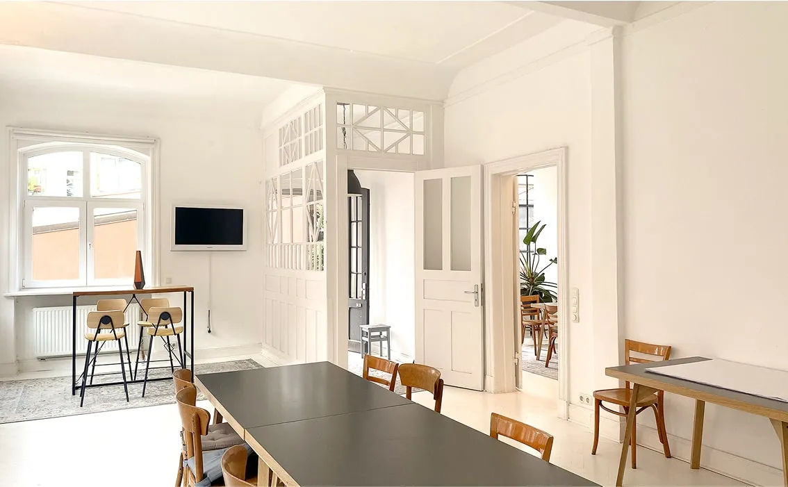 Kleiner Arbeitsbereich am Fenster – Dunkler Schreibtisch, Stuhl aus Rattan, dekorative Vase, viel Tageslicht.