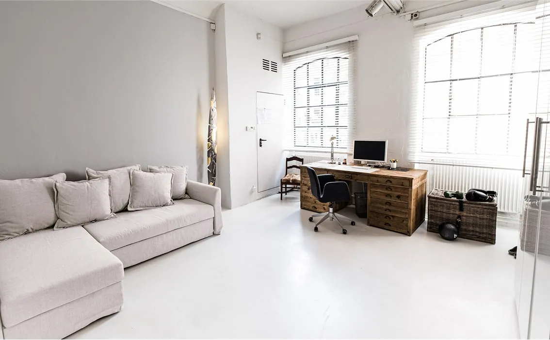 Moderner Arbeits- und Wohnbereich – Sofa, Schreibtisch und große Industriefenster mit viel Licht.