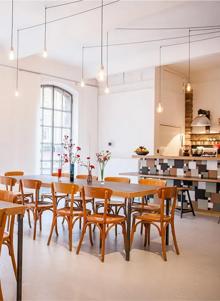 Heller Raum mit großen Fenstern, Holztischen und Stühlen – Eventlocation Hamburg für Seminare und Meetings.