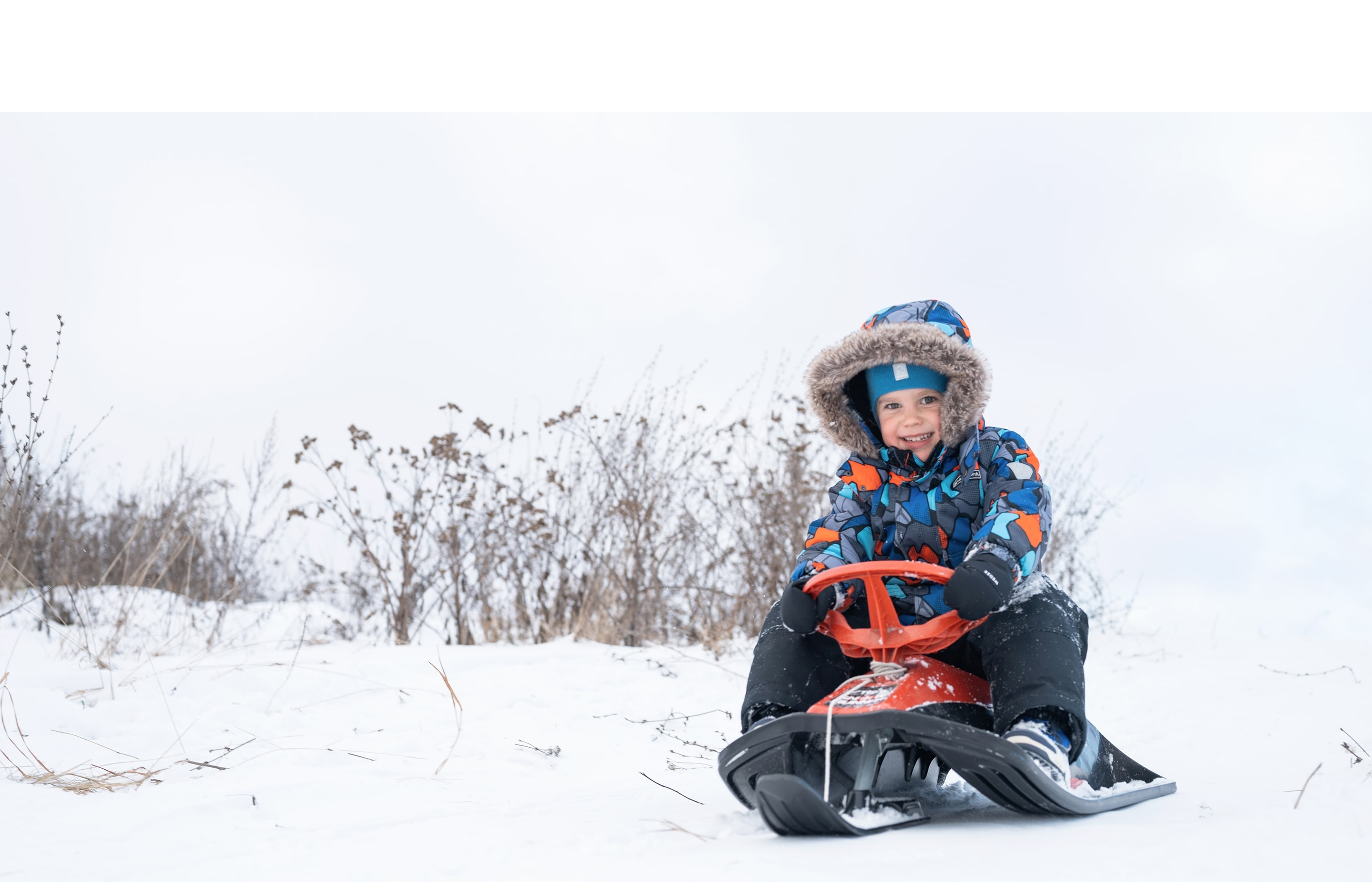 Happy five-year-old boy sledding down a snowy hill during winter holidays in Lapland.