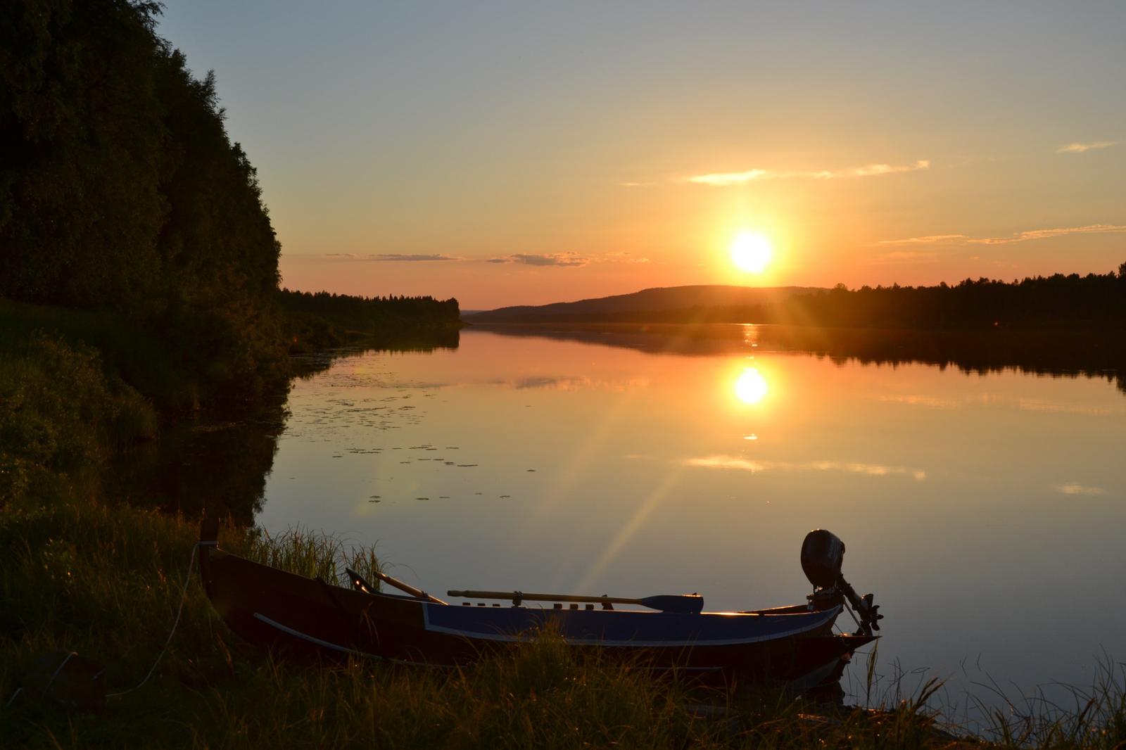 Sunset over a calm lake in Finnish Lapland with a small boat by the shore