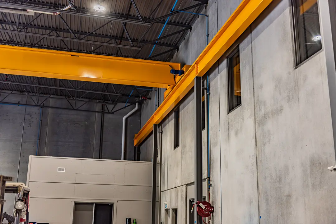 Bright yellow overhead crane system installed inside an industrial warehouse with concrete walls and steel roof framing.