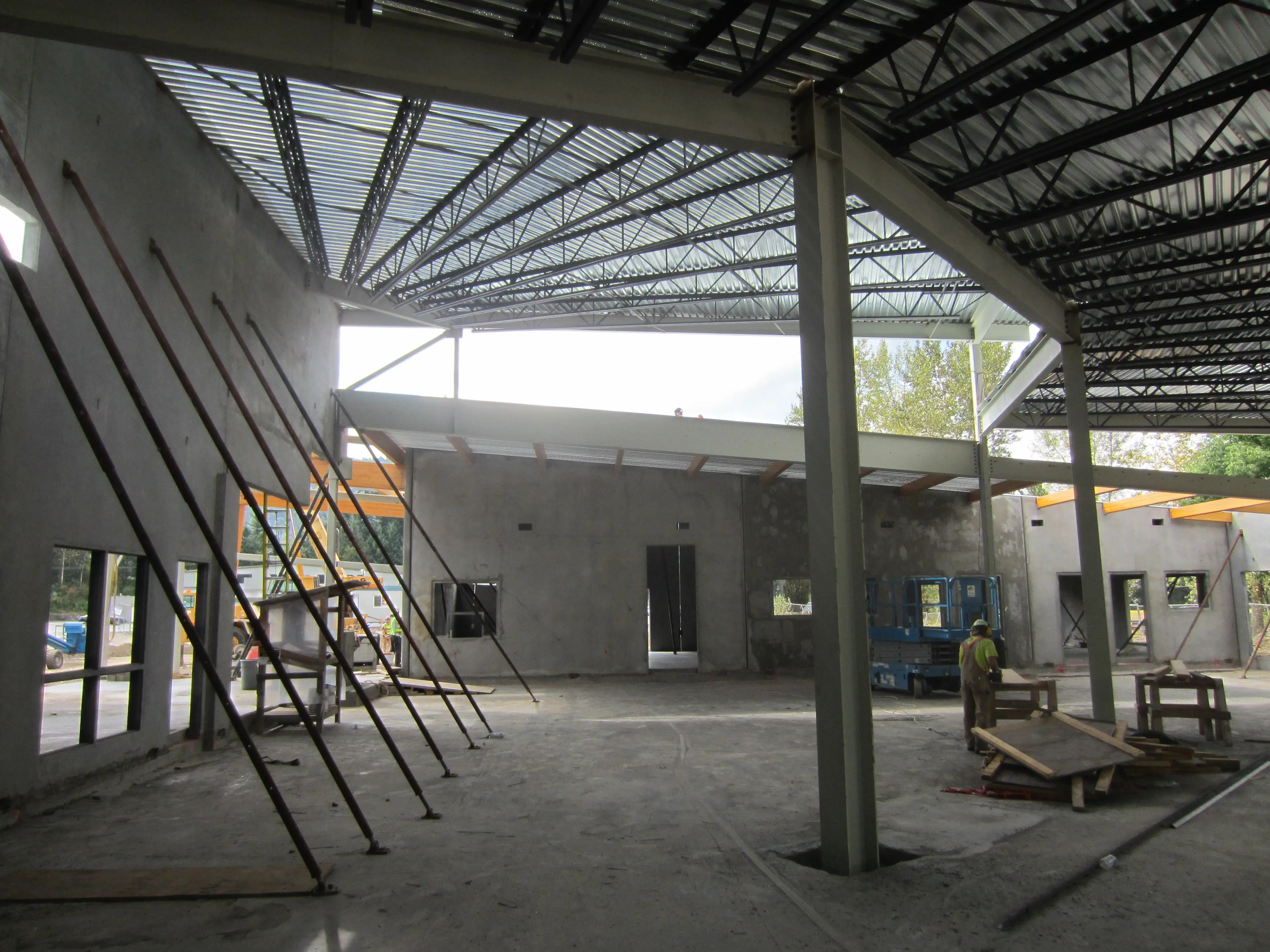 Interior view of a building under construction with exposed concrete walls, steel support beams, and bracing rods in place.