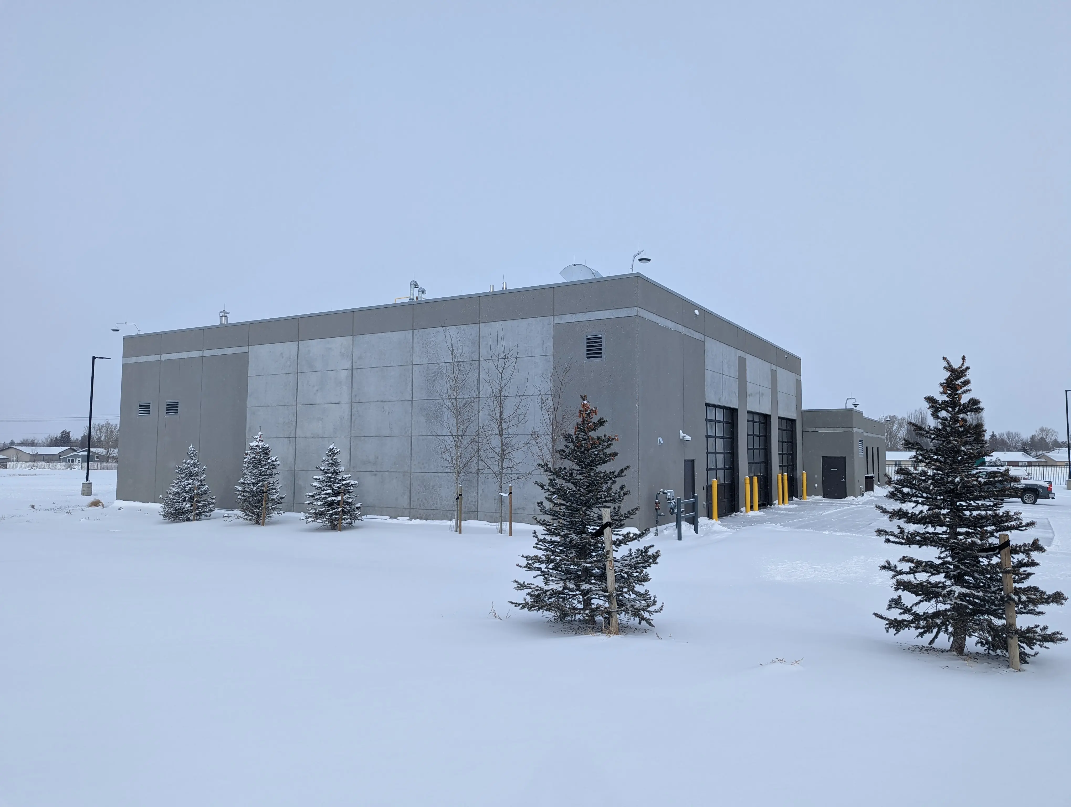 Exterior view of a modern fire hall building in winter, surrounded by snow-covered ground and pine trees.