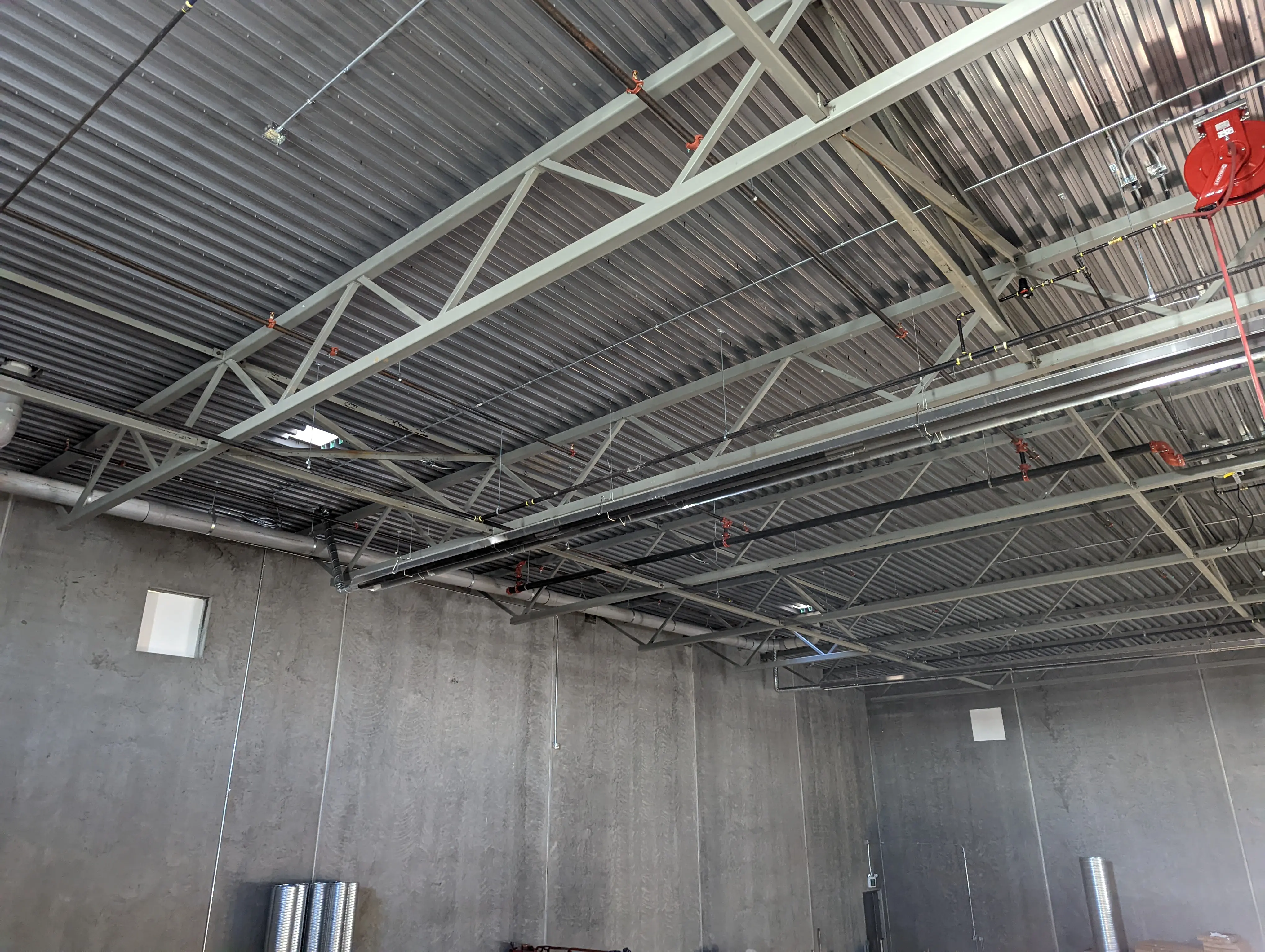 An upward view of the fire station’s metal truss ceiling system with visible utilities, fire suppression piping, and mechanical installations.