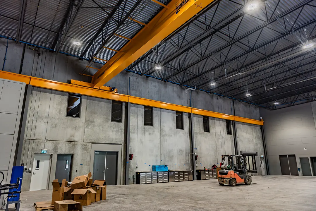 Close-up of a bright yellow overhead crane system with hoist and control cables suspended from the ceiling of a warehouse.