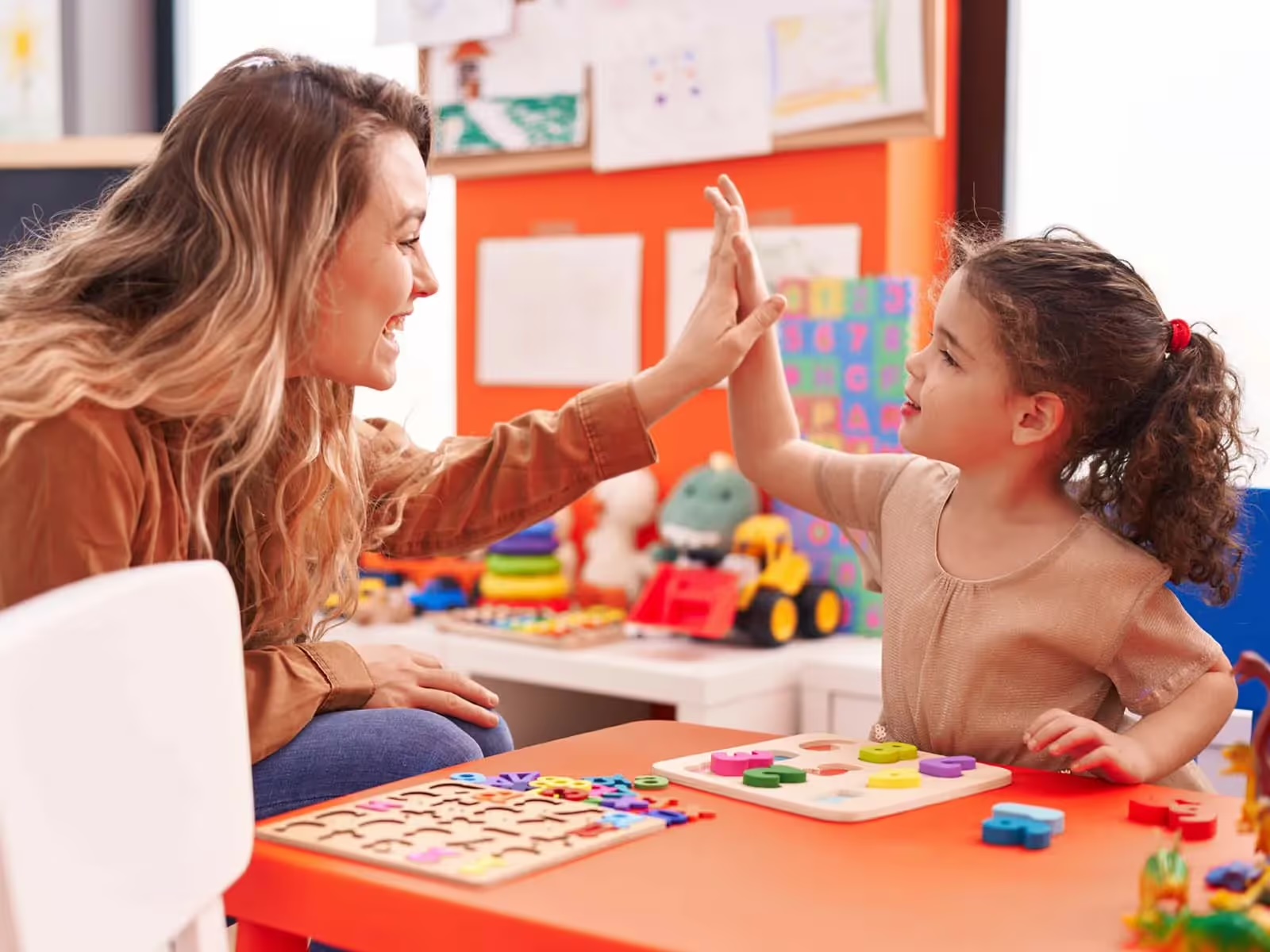 A young child and an adult high-five over developmental toys during a play-based learning session