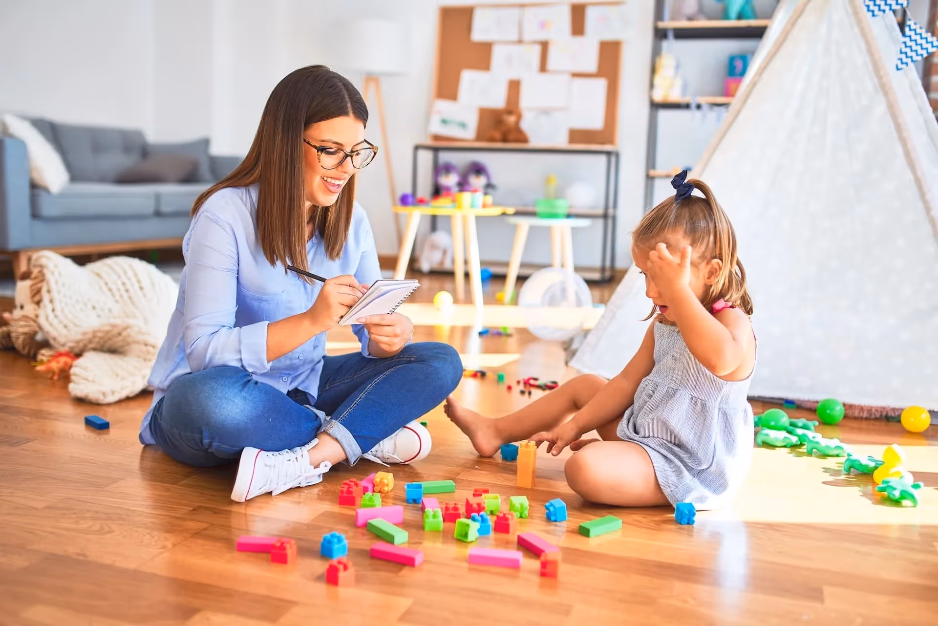 A clinician takes notes while observing a young child play during an autism evaluation
