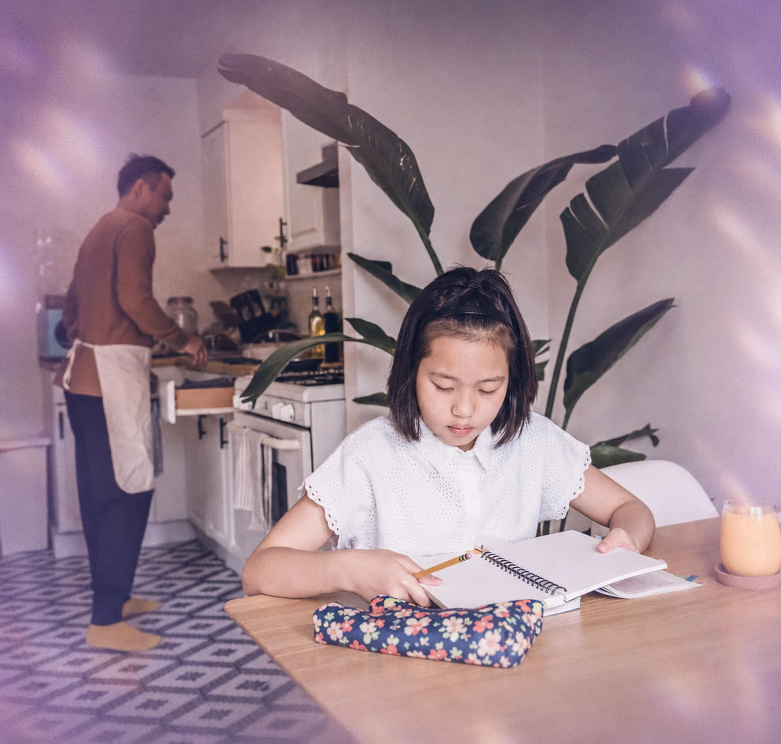 A child doing homework at the kitchen table while a parent cooks