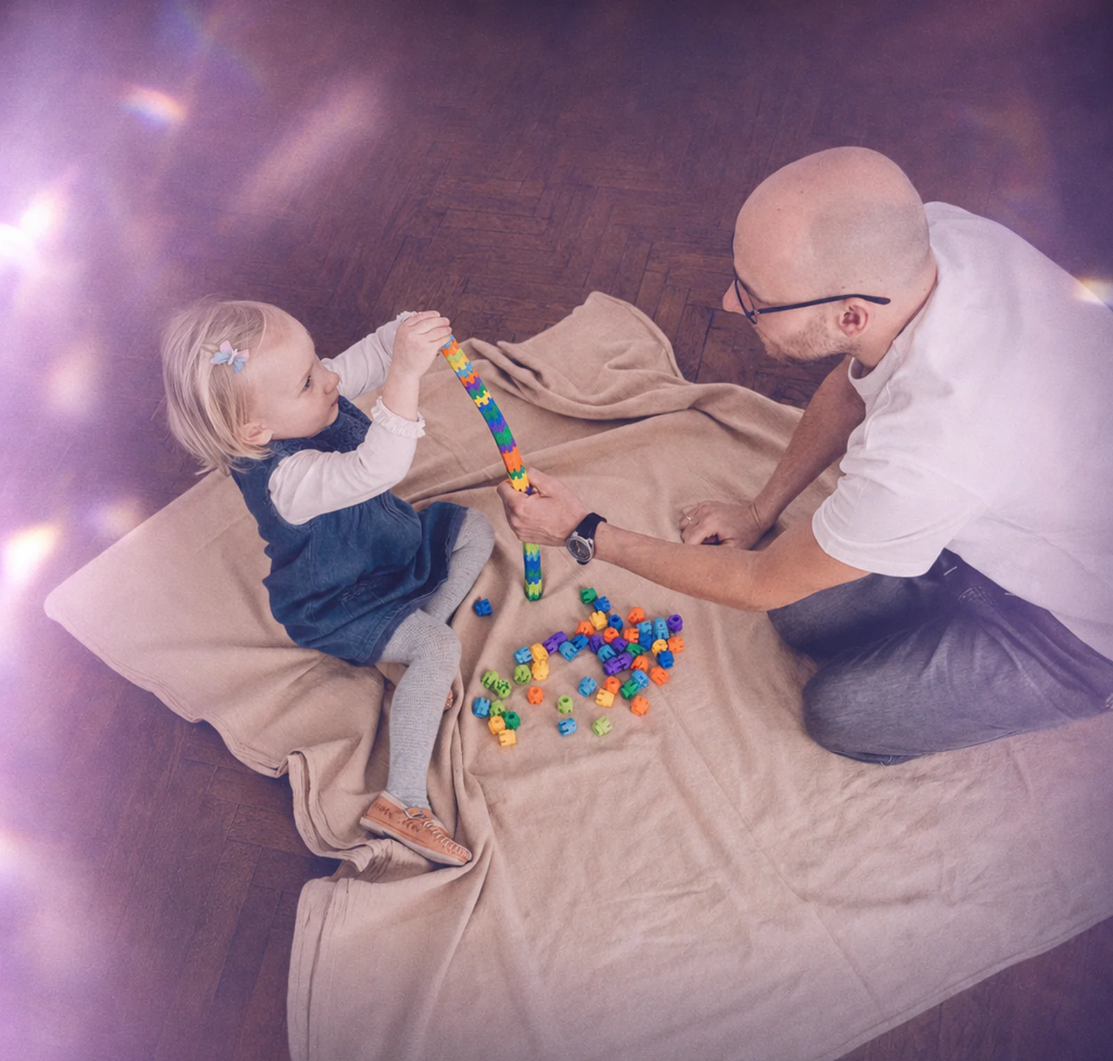 A parent and toddler building with wooden blocks on the floor