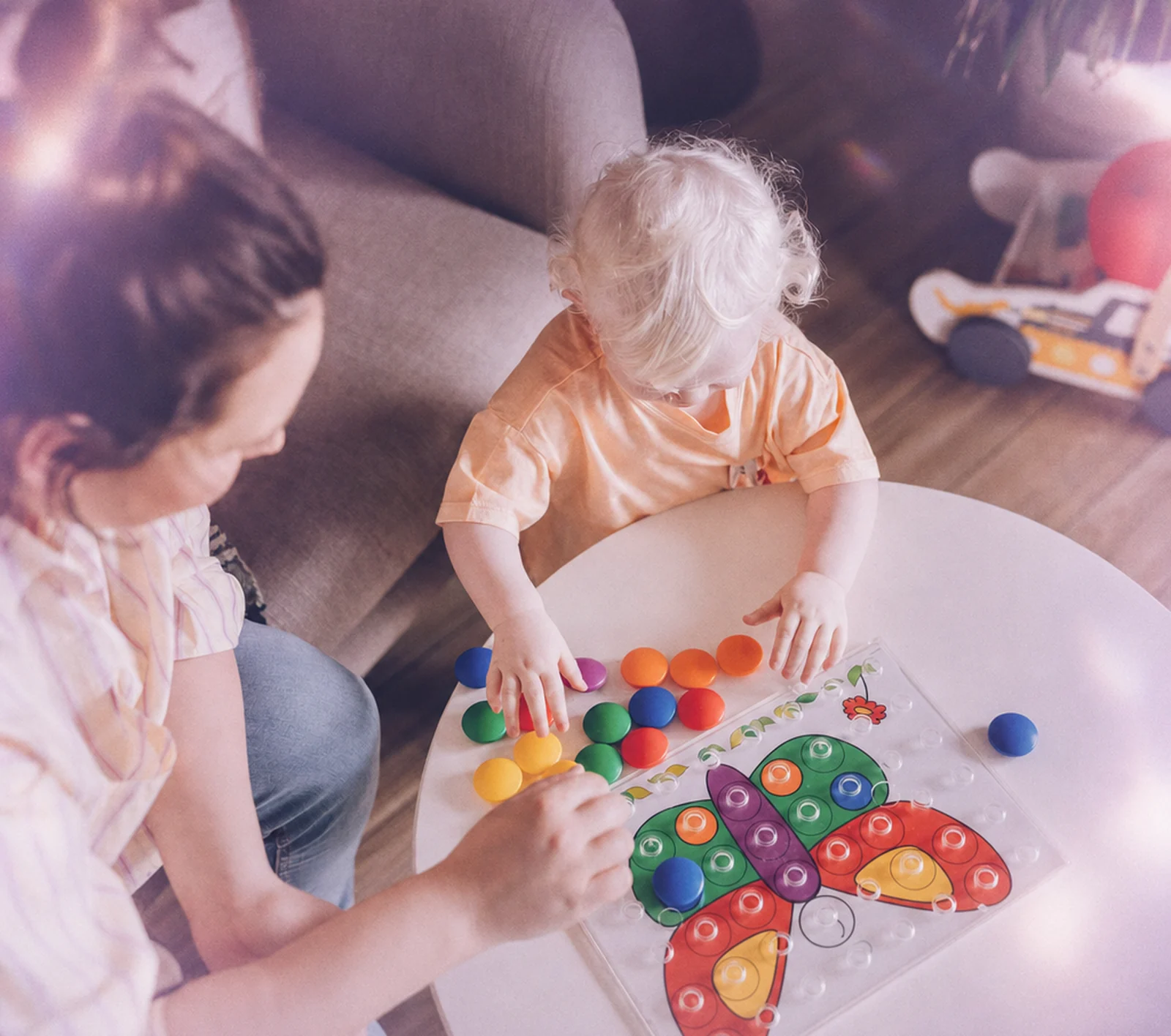 A parent waving during a virtual ABA session while her toddler plays beside her